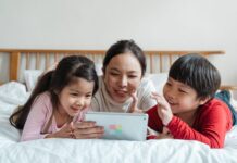 Mama z dwójką dzieci na łóżku bawiąca się tabletem